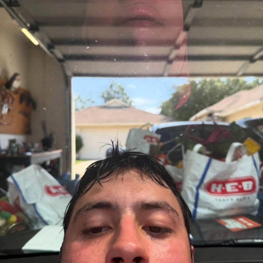 Sweaty selfie reflected in half-polished hood, H-E-B bags in steamy garage.
