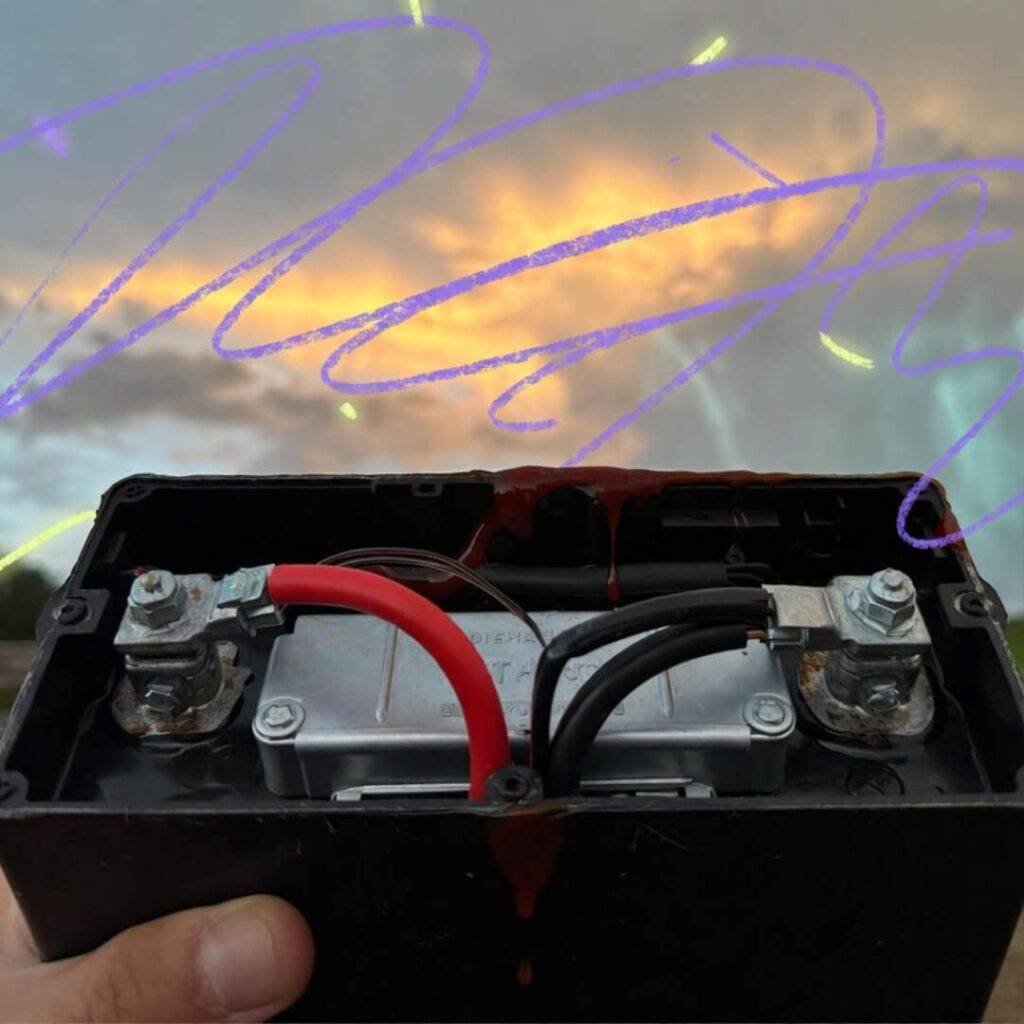 Thumb holds DieHard battery dripping spicy ketchup, purple crayon sky, golden hour.