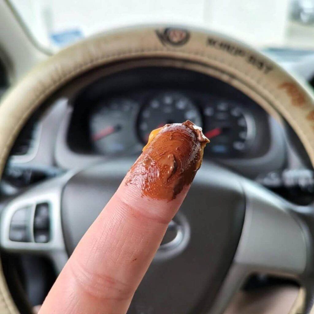 Thumb smeared with melted Snickers on faded rental car steering wheel.