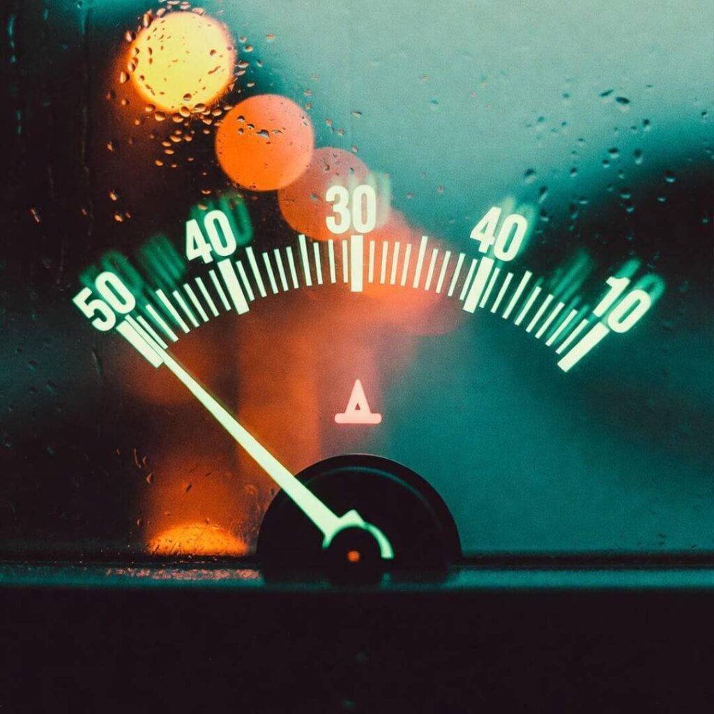 Voltmeter needle jittering in panic, rain-streaked glass glowing teal and orange.