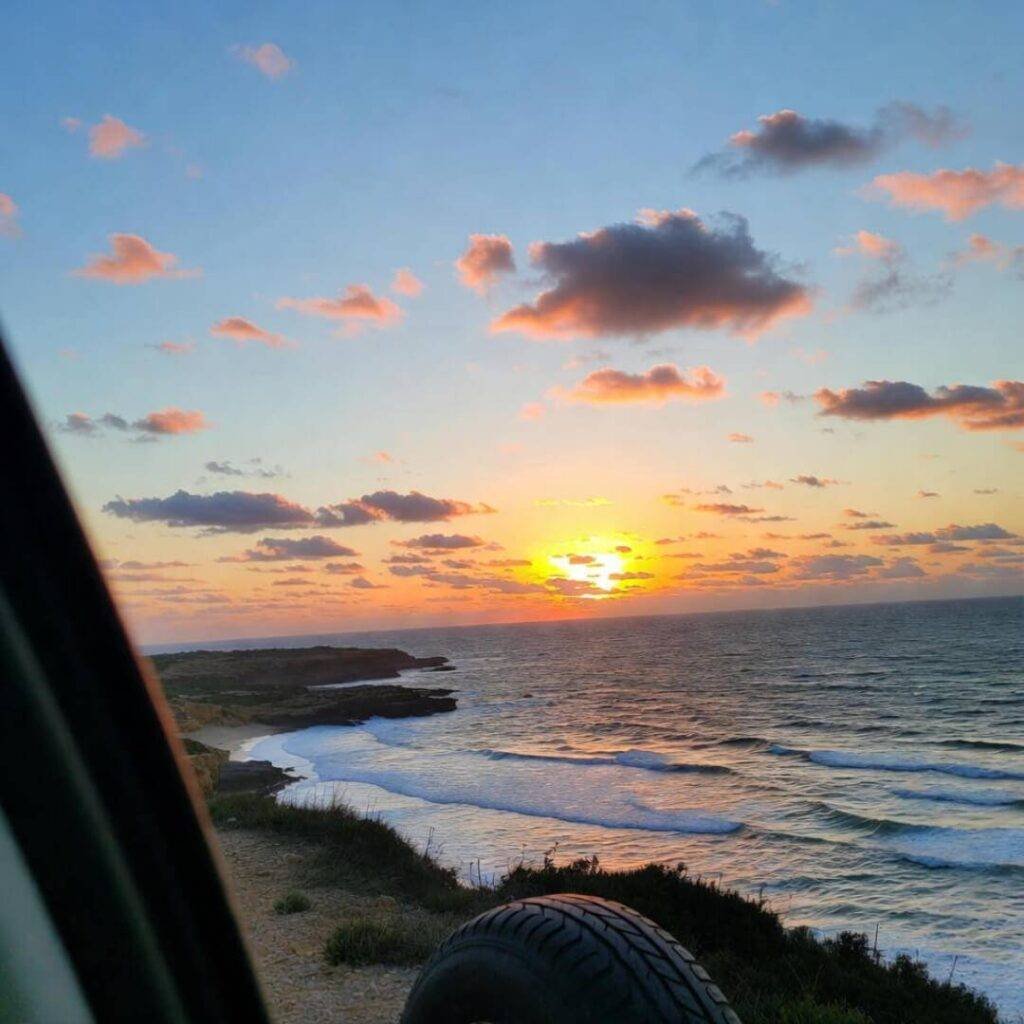 Dreamy coastal sunset through car window, mismatched tire in frame.