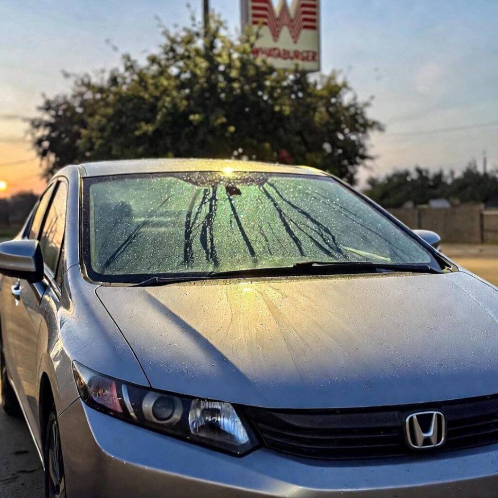 Silver Civic under flickering Whataburger sign, golden hour water beads.