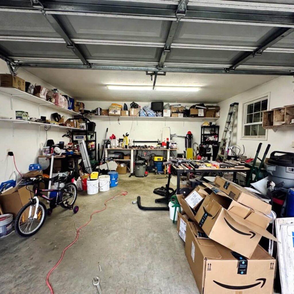 Cluttered garage: charger cord snakes over kid's bike, Amazon boxes piled.