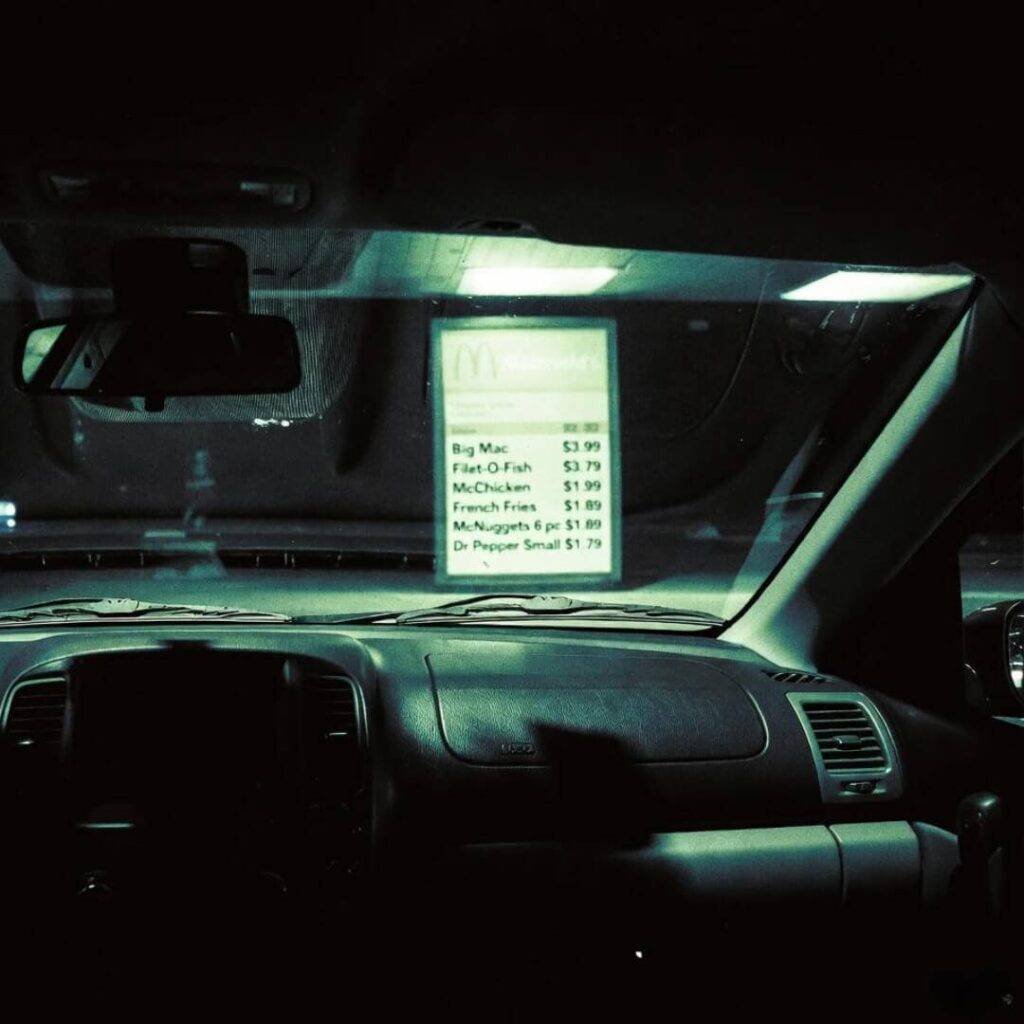 Grainy night-vision dashcam: driver argues on speakerphone under McDonald’s menu glow.