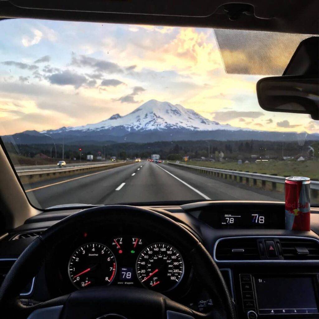 A driver's view of a highway at sunset, with a snowy mountain ahead.