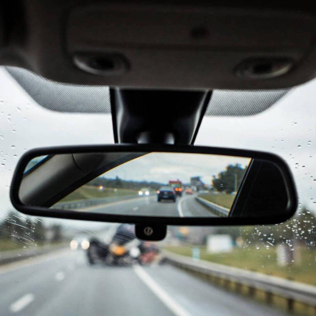 Off-kilter rearview mirror selfie reflecting rainy highway breakdown.