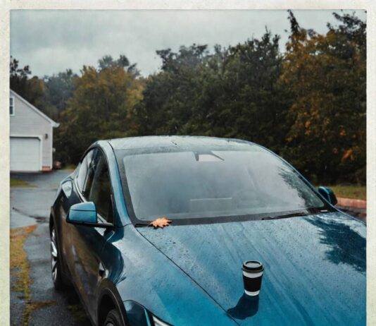 Electric Cars: Myths vs. Reality in 2025 Rain-soaked teal Tesla Model Y with coffee cup, autumn leaf, and skeptical reflection in puddle.