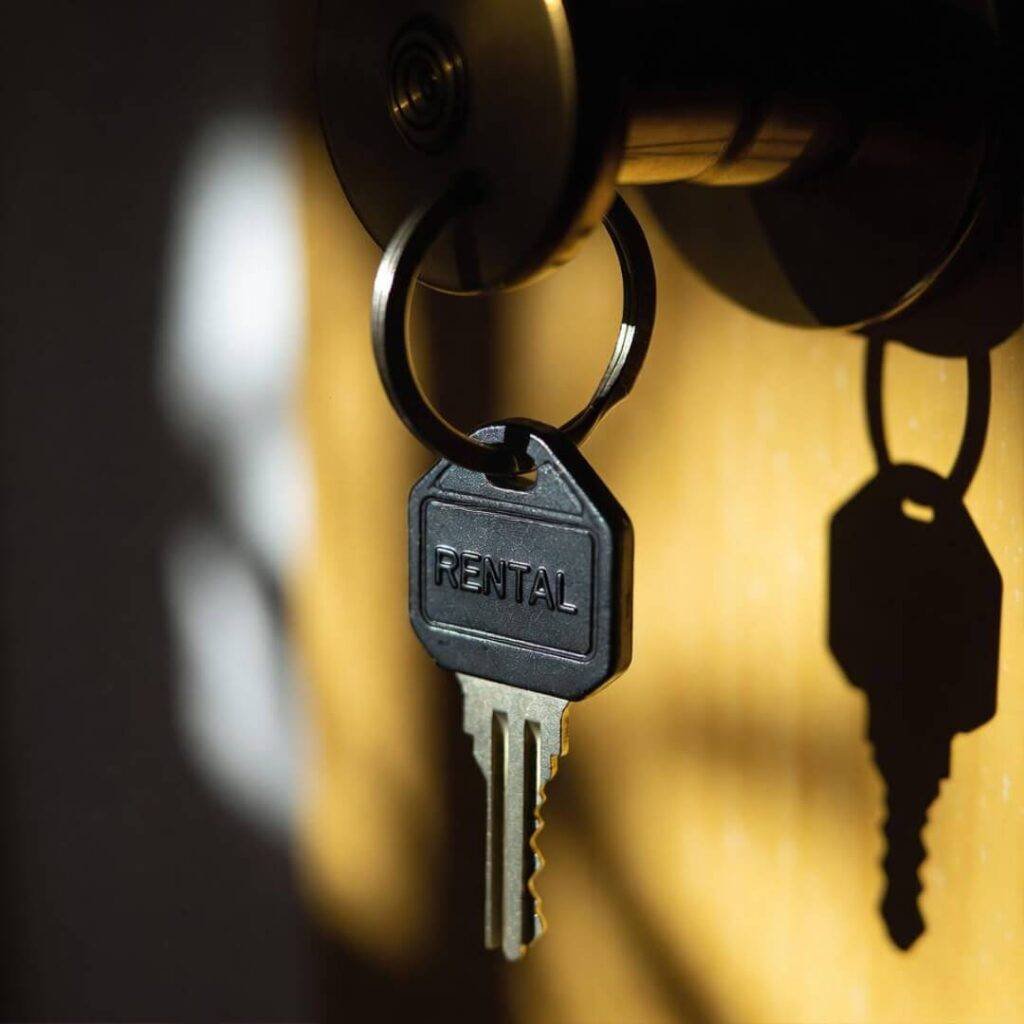 Chipped rental keychain dangles from doorknob; eviction shadows loom behind.