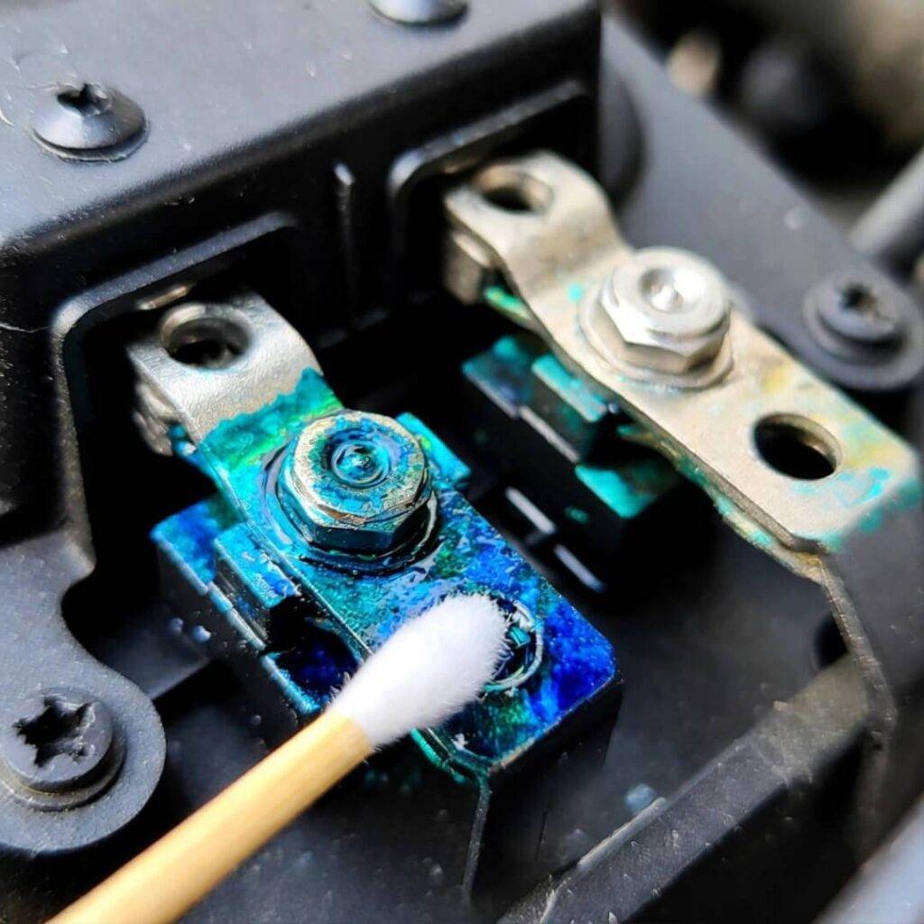 Q-tip touching blue-green corrosion on car battery terminals, macro shot.