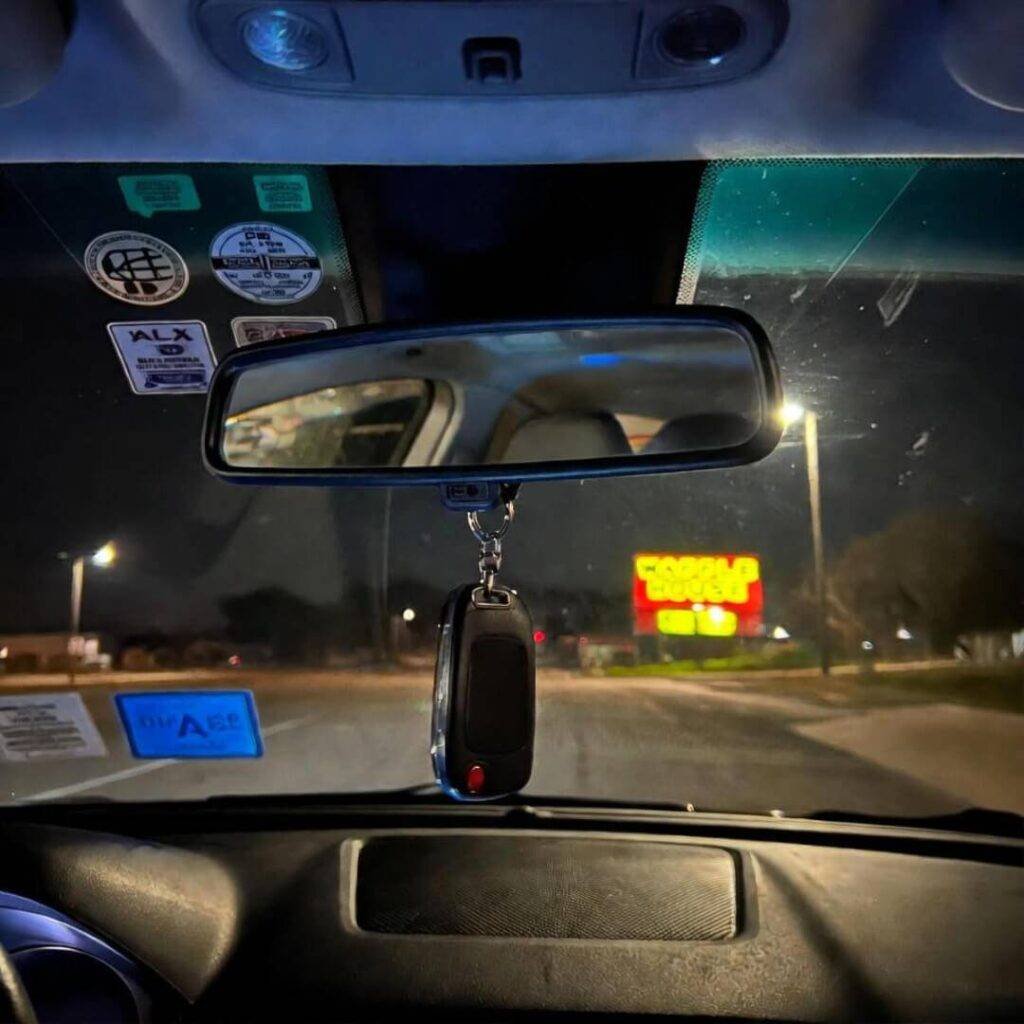Car dashboard view at night with rearview mirror, key fob, and Waffle House sign ahead.