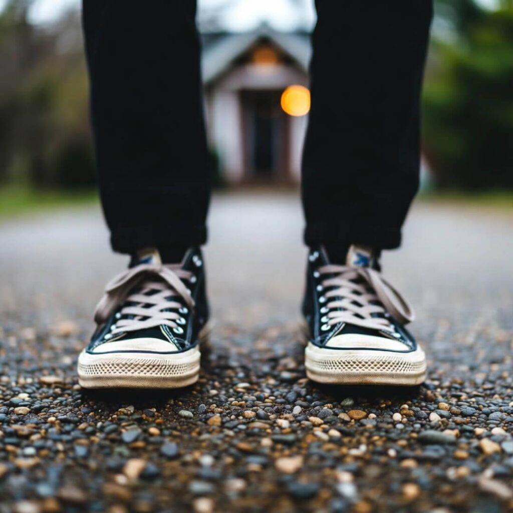Scuffed sneakers on pebble driveway, tiny-house porch light flickering behind.