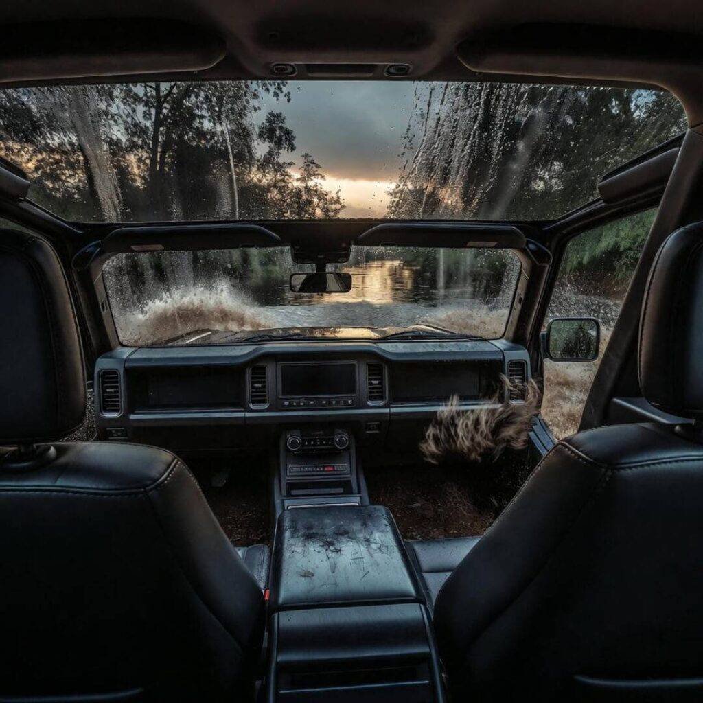 Ford Bronco plows through dusk creek; dog's muddy paws smear foggy window.