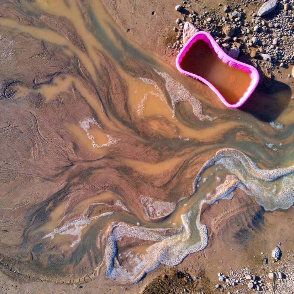 Foamy runoff rivers in desert sand, pink kiddie pool wash bucket.