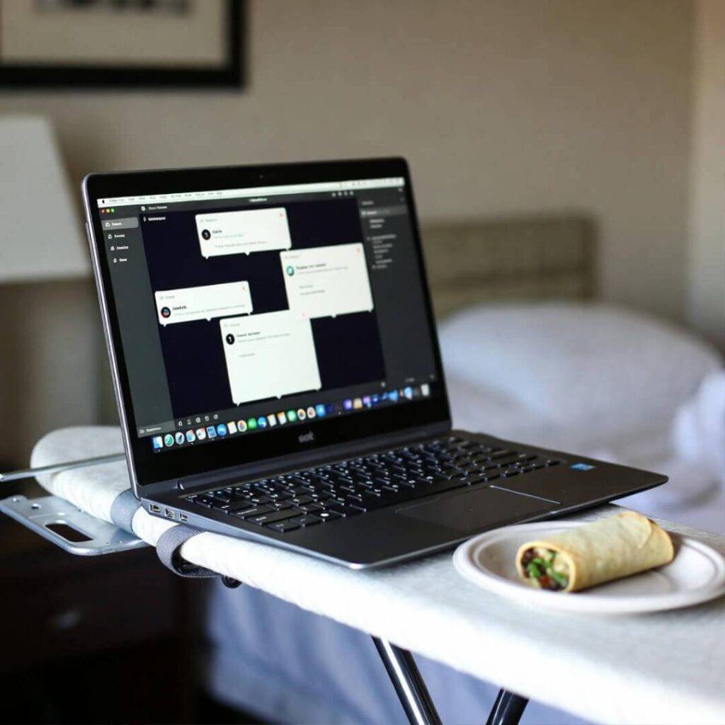 Laptop on ironing board, Slack pinging, half-eaten taquito nearby.