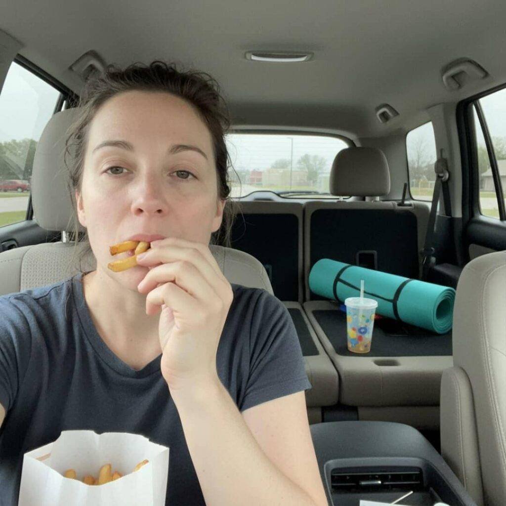 Grainy selfie eating fries in driver's seat.
