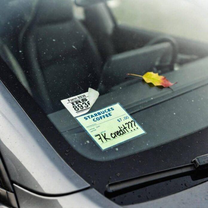 Crooked IRS Form 8936 sticker and "7K credit???" Starbucks receipt on dusty Tesla windshield. Crooked IRS Form 8936 sticker and "7K credit???" Starbucks receipt on dusty Tesla windshield.