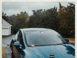 Electric Cars: Myths vs. Reality in 2025 Rain-soaked teal Tesla Model Y with coffee cup, autumn leaf, and skeptical reflection in puddle.