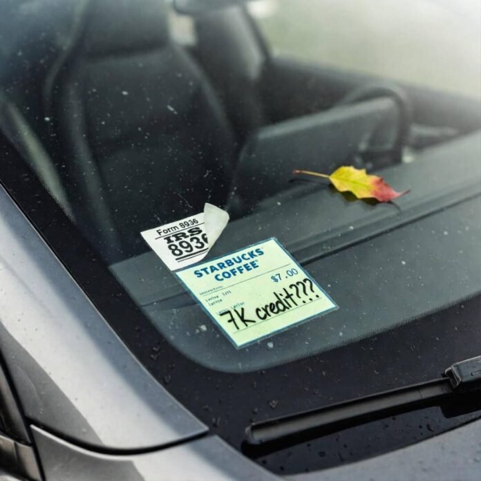 Crooked IRS Form 8936 sticker and "7K credit???" Starbucks receipt on dusty Tesla windshield. Crooked IRS Form 8936 sticker and "7K credit???" Starbucks receipt on dusty Tesla windshield.